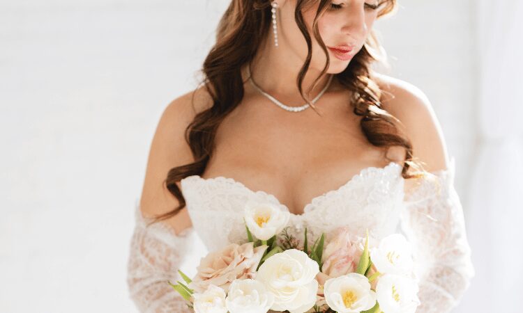 Close-up of a bride wearing an off-the-shoulder lace wedding dress holding a white bridal bouquet.
