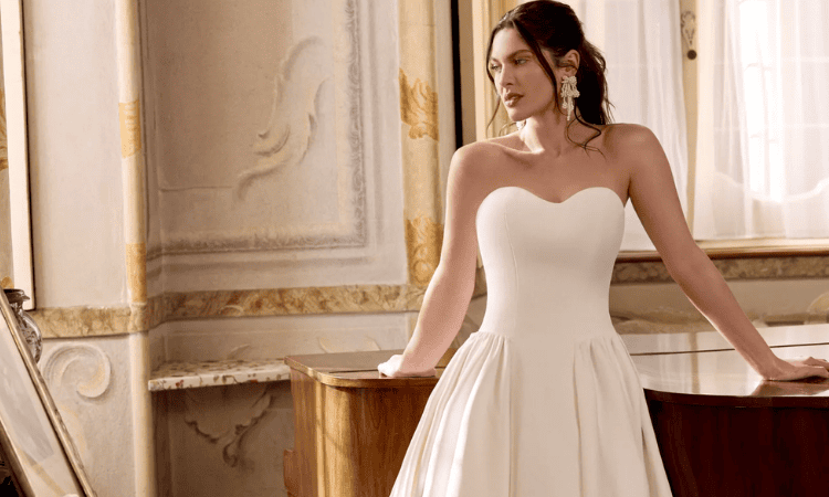 Bride wearing a strapless white wedding dress with a fitted bodice and flowing skirt in an elegant room.