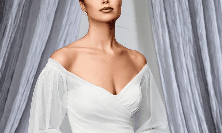 Bride wearing an off-the-shoulder wedding dress with a draped neckline and sheer long sleeves.