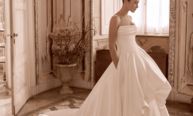 Bride wearing a strapless white wedding dress with a draped bodice and full, flowing A-line skirt in an elegant room.
