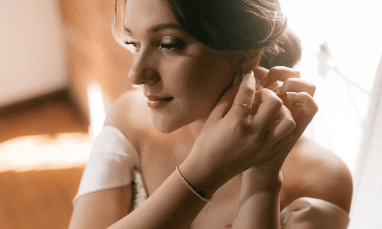 Bride adjusting her earring while wearing an off-the-shoulder wedding dress.