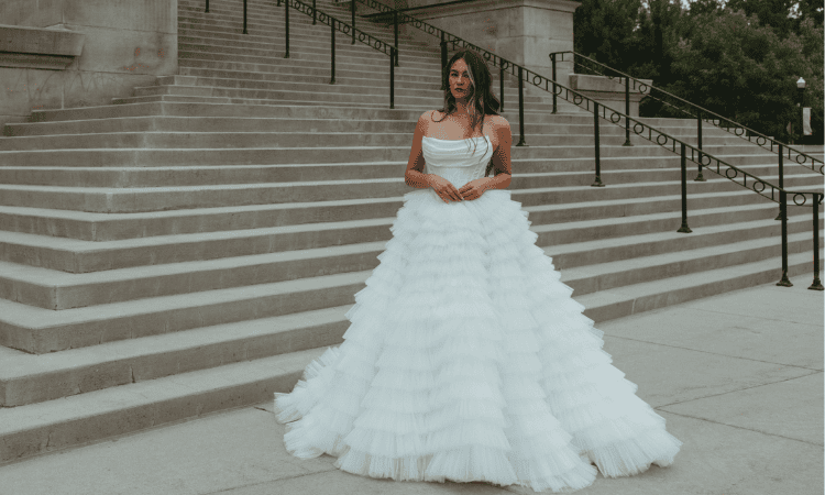 Bride wearing a strapless ball gown with a full tiered tulle skirt, standing on grand outdoor steps.