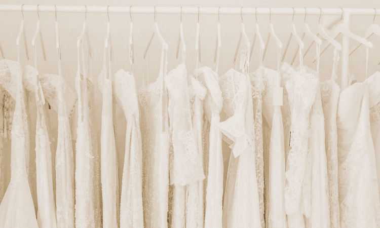 Wedding dresses hanging on a rack, featuring a variety of white gowns with lace, fitted, and flowing designs.