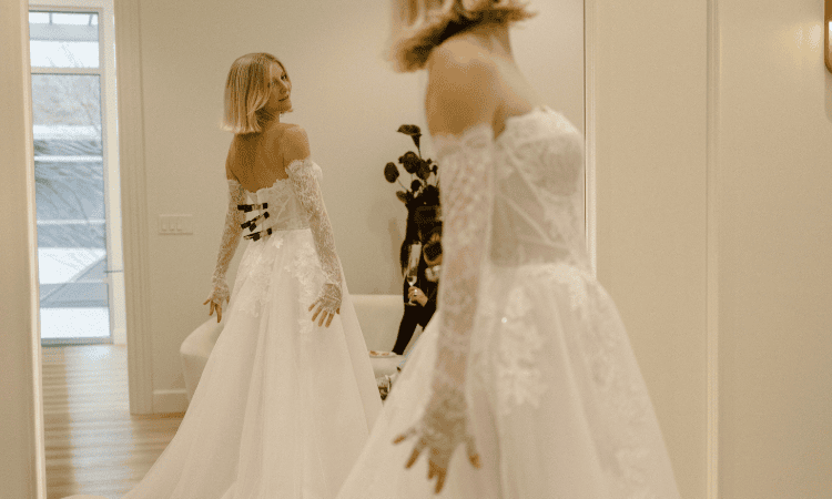 Bride in a lace wedding dress looking at her reflection in a full-length mirror.